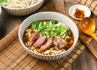 Tipik acı biber soslu biftek tendon eriştesi, taze soğan, ahşap kaşık ve yemek çubukları Tayvan yemeklerinin yanında servis edilir.