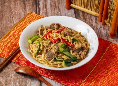 Kırmızı biberli kızarmış şehriye, yemek çubuğu ve kaşıkla servis edilen peçete manzaralı, Tayvan yemeklerinin ahşap masasında.