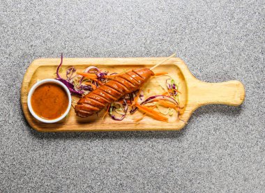 Biber soslu jumbo sosis Hong Kong fast food 'un gri arka planında izole edilmiş ahşap ozan üzerinde servis edilir.