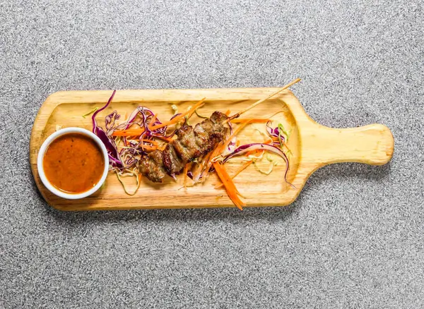 Kırmızı biber soslu domuz bbq satay, Hong Kong fast food 'un gri arka planında izole edilmiş ahşap ozanda servis edilir.