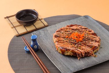 Mentaiko Octopus Okonomiyaki, Japon yemeklerini arka planda izole edilmiş yemek çubuklarıyla servis ediyor.