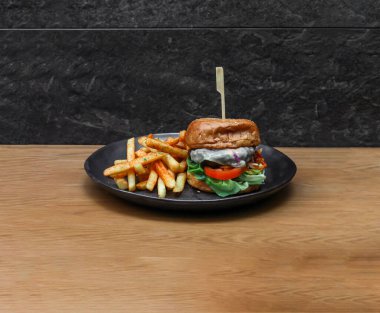 Çimenli Beef Burger ve patates kızartması, tahtadan masa başında İtalyan fast food manzarası ile servis ediliyor.