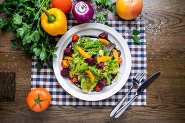 Portakallı pancar kökü salatası, ıspanak, domates, soğan, kapsika, kişniş, bıçak ve çatal peçetede servis edilir. Tahta masa üzerinde domates, soğan, kapsika, kişniş, bıçak ve çatal servisiyle servis edilen İtalyan fast food peçetesinin üstünde servis edilir.