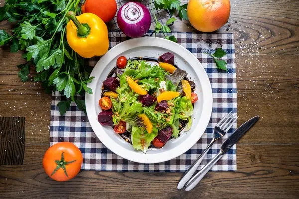 Portakallı pancar kökü salatası, ıspanak, domates, soğan, kapsika, kişniş, bıçak ve çatal peçetede servis edilir. Tahta masa üzerinde domates, soğan, kapsika, kişniş, bıçak ve çatal servisiyle servis edilen İtalyan fast food peçetesinin üstünde servis edilir.