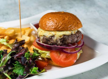 Wagyu Biftek Burger, domates, soğan, lahana ve patates kızartması... İtalyan yemeğinin arka planında servis edilir.