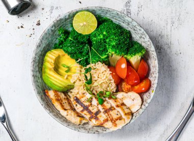 Izgara tavuk göğsü kasesi brokoli, mısır, marul, kızarmış pirinç ve limon. Arka planda izole edilmiş İtalyan yemeği manzarasında servis ediliyor.