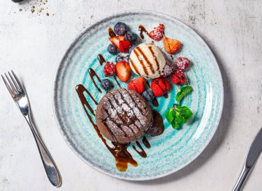 Erimiş çikolatalı puding vanilyalı dondurma, çilekli, yaban mersinli ve nane arkaplanda izole edilmiş tabakta servis edilen İtalyan yemeği.