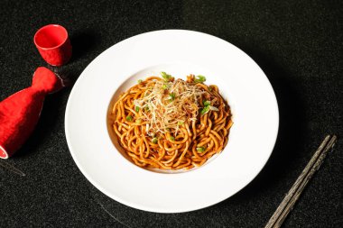 Soya ve Scallion yağlı erişteler yemek çubuklarıyla servis ediliyor. Arka planda koyu renk Hong Kong yemeklerinin üst görüntüsü.