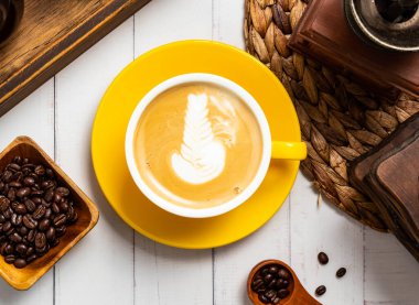 Karışık Latte Sanatı ile kremalı Cappuccino taze kavrulmuş kahve çekirdekleri ve Tayvan kahvesi sıcak içeceği masasının üstünde izole edilmiş ahtan bir kaşık ile canlı sarı bir fincanda servis edilir.