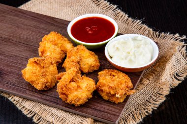 Ahşap tahtada servis edilen domates soslu ve mayonez soslu gevrek hindistancevizi karidesi koyu arkaplanda peçete tarafından izole edilmiş fast food manzarası.