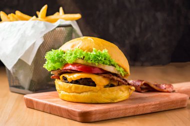 Marul, domates, soğan ve peynirli sığır pastırmalı çizburger tahtadan izole edilmiş patates kızartması sepeti ve fast food manzaralı.