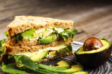 Avokado ve Yumurta Kulübü Sandviçi, sağlıklı yiyeceklerin yakın çekim masasında servis edilir.