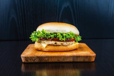 Marul, Domates ve Peynirli klasik tavuk çizburgeri. Tahta tahta tahta tahta üzerine izole edilmiş, arka planda fast food manzaralı.