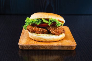 Marul, domates ve peynirli çıtır tavuk fileto. Tahta tahtada, arka planda fast food manzarası var.