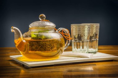 Naneli Sencha Green çayı Buharlı Çaydanlık 'ta servis edilir. Bardaklar ve çay poşeti izole edilir. Tahta masa manzaralı sıcak çay.