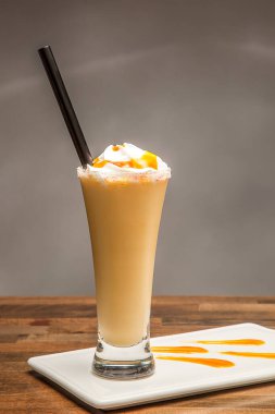 Tuzlu Karamelli Mango milkshake, çırpılmış krema ve çiseleyen cam. Tahta masa kenarında izole edilmiş soğuk içecekler.