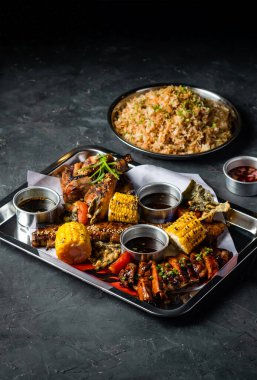 Izgara et, sarımsaklı pilav, ızgara mısır koçanı, Peri Peri Tavuğu, Jerk Chicken, Biftek Göbeği Göğüs eti, Soğan ve Sos ile donatılmış tepside servis edilen gri arka plan manzarası