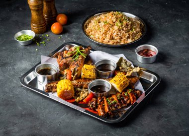 Izgara et, sarımsaklı pilav, ızgara mısır koçanı, Peri Peri Tavuğu, Jerk Chicken, Biftek Göbekli Göğüs eti, Domates ve Sos ile Filipin ziyafeti, izole edilmiş gri arka plan tabağı servis edildi.