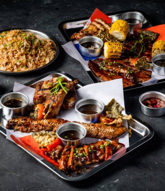 Izgara et, sarımsaklı pilav, ızgara mısır koçanı, Peri Peri Tavuğu, Jerk Chicken, Biftek Göbeği Göğüs eti, Domuz göbeği, domates ve soslu tepsi yanında servis edilen soslar.