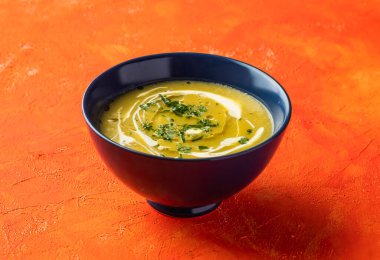 Kremalı kavrulmuş balkabağı çorbası, mantar ve kişniş, portakal rengi arka planda izole edilmiş sıcak içecek manzarasıyla servis edilir.