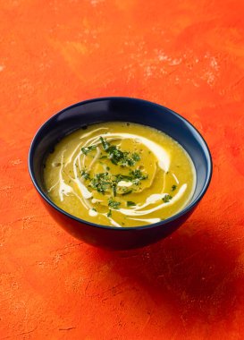 Mantarlı kremalı balkabağı çorbası ve kişniş, turuncu arka planda izole edilmiş bir kasede servis edilir. Sıcak içeceğin yakın plan görüntüsü.