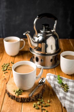 Sıcak süt çayı, Masala Chai, Karak Çay Saati çaydanlık ve kakule ile servis edilir. Tahta masa kenarında sıcak içecek manzarası izole edilir.