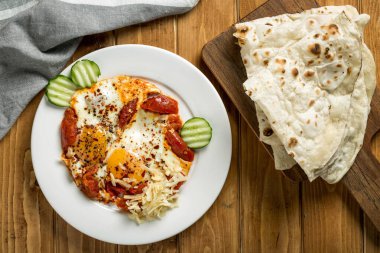 Tabakta servis edilen domatesli yumurta ve pita ekmeği ahşap masa üzerinde Arap yemeğinin üst görüntüsünde.