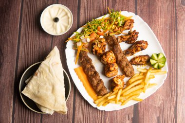 Türk usulü ızgara tavuk, şiş tawook, tavuk kebabı, ouzi tavuğu, sığır eti Adana, pita ekmeği, humus ve patates kızartması ahşap masa üzerinde servis ediliyor.