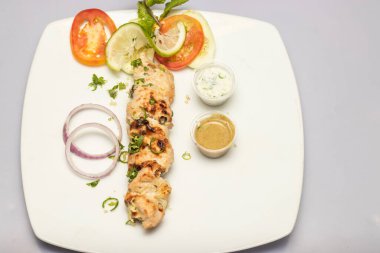 Malai Tikka Boti tavuğu ya da salata ve baharat soslu Reshmi kebabı gri arka planda, Bangladeş, Hint ve Pakistan yemeklerinin üst manzarasında servis edilir.