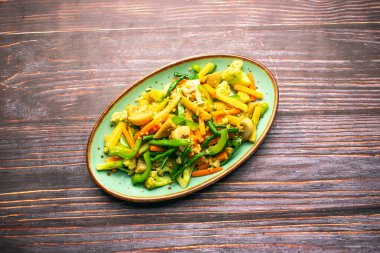 Sotelenmiş sebzeler arasında havuç, bebek mısır, kapsiyum, mantar, karnabahar ve ahşap masa üzerinde izole edilmiş tepsi tabağında servis edilen yeşil biber, bangladeş ve Tayland yemekleri yer alıyor.