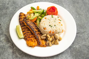 Kızarmış pilavlı ızgara balık ve sebze salatası servis edilir. Gri arka planda, Asya yemeğinin arka planında izole edilmiş.