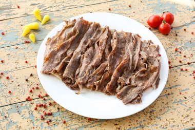 Porsiyon Doner kebabı eti, ahşap masada servis edilen domatesli, Arapça ve Türkçe fast food manzaralı.