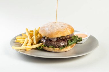 Kızartmalı ve mayonezli klasik sığır burger. Beyaz arka planda servis edilen Amerikan yemeğinin yanında servis ediliyor.