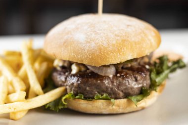 Kızartmalı ve mayonezli klasik sığır burger, beyaz masa ve siyah arka planda izole edilmiş tabakta servis edilir.