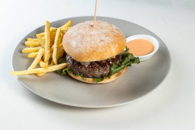 Kızartmalı ve mayonezli klasik biftek burgeri beyaz arka planda servis edilir.