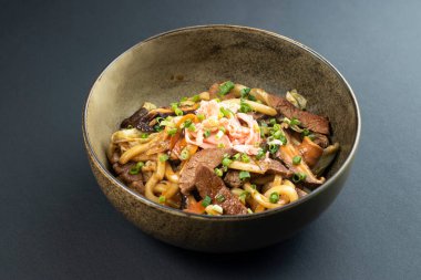 Biftek Yakisoba Eriştesi, üstü yeşil soğanla kaplanmış. Japon fast food 'unun koyu arka planında izole edilmiş.