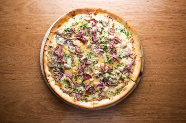 Kremalı mantar ve kremalı beyaz soslu pastırmalı pizza ve eritilmiş peynir İtalyan kuzeninin arka planında izole edilmiş ahşap tahtada servis ediliyor.