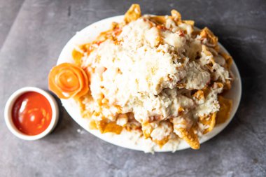 Tepside ketçaplı tavuk nachos servis ediliyor. Gri arka planda Hint, Bangladeş ve Pakistanlı yiyeceklerin üst görüntüsü var.