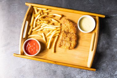 Tahta tepside servis edilen mayonez soslu kızarmış balık ve patates kızartması. Gri arka planda Hint, Bangladeş ve Pakistanlı yiyeceklerin üst görüntüsü.