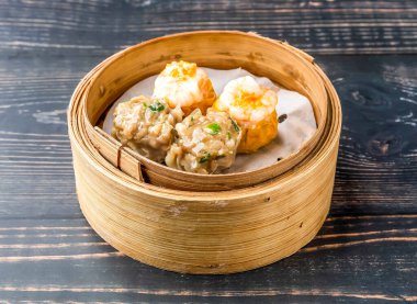 Domuz eti ve karides Siomai bambu buharlı tencerede servis ediliyor. Tahta masa başında Hong Kong yemeği manzarası var.