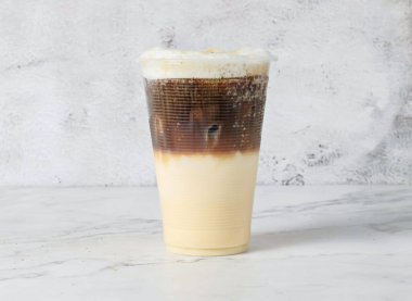 Buzlu kopi cino katmanlı buzlu kahve içeceği Singapur meşrubatının arka planında izole edilmiş plastik bardakta servis edilir.