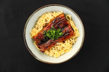 Unagi Don, pirinç erişteli ızgara yılanbalığı ve yeşil soğanla süslenmiş Japon kuzeninin üst masasında tek başına servis edilen tabakta.