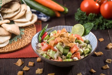 Tahta masadaki bir kasede servis edilen yağlı salata, Pita ekmeği parçaları, taze sebzeler ve sağlıklı Orta Doğu salatasının yan görünüşü.