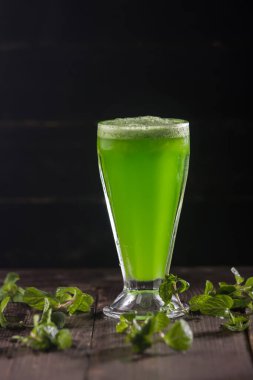 Taze Limon Nane Suyu, koyu arkaplanda taze nane yaprakları ve ferahlatıcı ve sağlıklı narenciye içeceği için ahşap masa manzaralı uzun bir bardakta servis edilir.