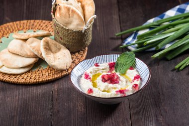 Mutabal, üzerinde nar tohumları ve klasik Orta Doğu aperatiflerinin taze nane şekeri olan tahtadan bir masada pide ekmeği olan bir kasede servis edilen kremalı patlıcan sosu.
