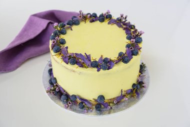 Çiçek desenli limonlu yaban mersinli kek, yaban mersinli açık sarı bir krema ve peçete manzaralı çiçekli, kutlamalar için mükemmel bir pasta içeriyor.