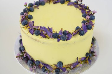 Çiçek desenli limonlu yaban mersinli kek, yaban mersinli ve çiçekli açık sarı bir krema ve kutlama için mükemmel bir pasta manzarası içeriyor.