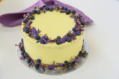 Çiçek desenli limonlu yaban mersinli pasta, kutlamalar için mükemmel peçete manzaralı yaban mersinli ve çiçekli açık sarı bir krema içeriyor.