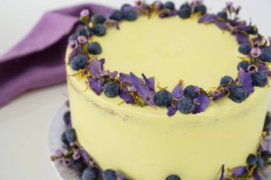 Çiçek desenli limonlu yaban mersinli kek, yaban mersinli açık sarı krema ve peçeteli çiçekli süslemeli, kutlamalar için mükemmel zarif bir pasta.