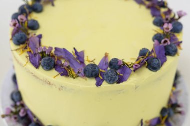 Çiçek desenli limonlu yaban mersinli kek, yaban mersinli ve çiçekli açık sarı bir krema ve yakın çekimde, kutlamalar için mükemmel cafe keki.